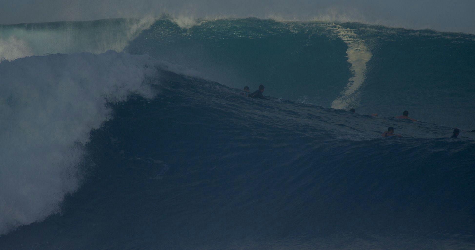 Surfers paddle for the shoulder as a Second Reef set wave begins to break.