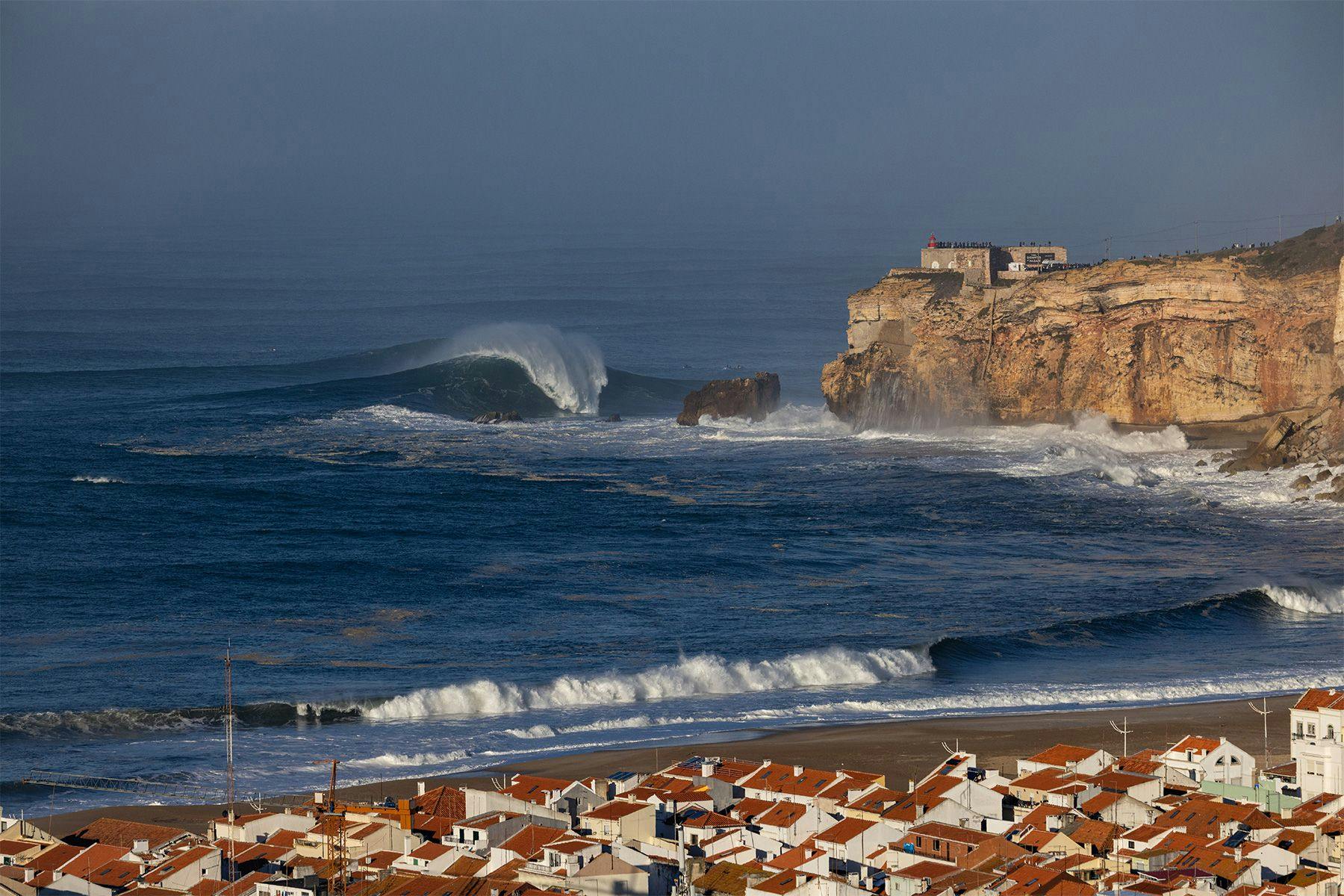 big wave breaking beneath the lighthouse at nazare in portugal