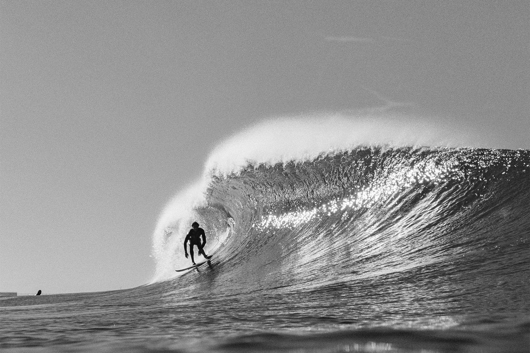 blaack and white 35mm photograph of a surer dropping into a large lefthand wave, photographed on a nikonos camera by grant musso